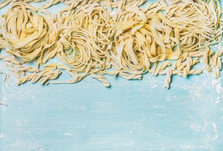 Various homemade fresh uncooked Italian pasta with flour on blue wooden background, top view, copy space, horizontal compositionの写真素材
