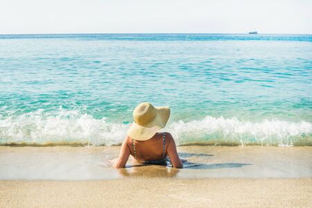 Tanned tourist woman in swimsuit and hat lying on sand and enjoying clear blue waters of Mediterranean sea at Cleopatra beach, Alanya, Mediterranean region, Turkeyの写真素材