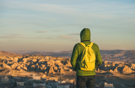 Young man traveller wearing bright clothing and yellow backpack standing and watching sunrise in the mountains over Goreme, Cappadocia, Central Turkeyの写真素材