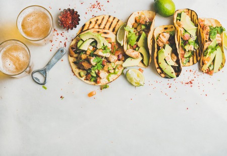 Healthy corn tortillas with grilled chicken, avocado, fresh salsa, limes and beer in glasses over...