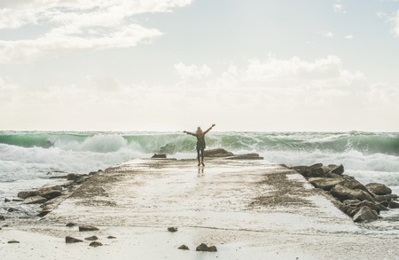 Young woman tourist standing on pier and enjoying waves of stormy Mediterranean sea in winter with raised hands, Alanya, Turlkeyの写真素材