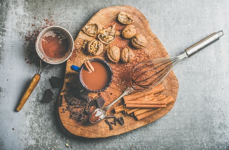 Rich winter hot chocolate with cinnamon sticks and walnuts in blue enamel mug on wooden board over grey concrete background, top viewの写真素材