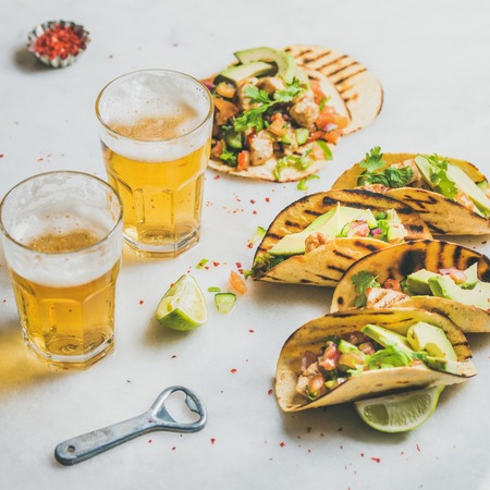 Healthy corn tortillas with grilled chicken fillet, avocado, fresh salsa, limes, beer in glasses over light grey marble background, selective focus, square crop. Gluten-free, weight loss conceptの写真素材