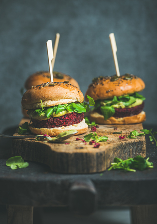 Healthy vegan burgers with beetroot and quinoa patty, arugula, avocado sauce, wholegrain buns on rustic wooden board over dark table, plywood background, selective focus. Dieting conceptの写真素材
