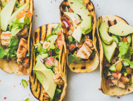 Healthy corn tortillas with grilled chicken fillet, avocado, fresh salsa, limes over light grey...