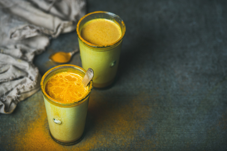 Golden milk with turmeric powder in glasses over dark grunge background, copy space. Health and energy boosting, flu remedy, natural cold fighting drink. Clean eating, detox, weight loss conceptの写真素材