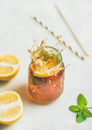 Summer cold Iced tea with fresh bergamot, mint and lemon in glass jar with splashes on light table background. Food in motion conceptの写真素材