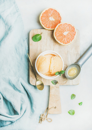Pink grapefruit homemade sorbet with fresh mint leaves in white bowl on wooden board over light grey background, top view. Fresh healthy raw vegan summer dessert conceptの写真素材