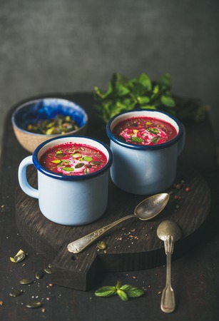 Spring beetroot soup with mint, pistachio, chia, flax, pumpkin seeds in blue enamel mugs over dark wooden background, copy space. Clean eating, healthy, vegetarian, vegan, dieting, weight loss conceptの写真素材