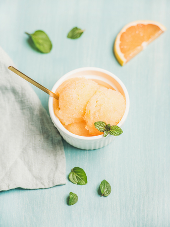 Pink grapefruit sorbet with fresh mint leaves in white bowl over blue painted background, selective focus. Fresh healthy raw vegan summer dessert conceptの写真素材