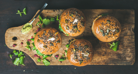 Healthy vegan burger with beetroot and quinoa patty, arugula, avocado sauce, wholegrain bun on rustic wooden board over dark wooden background, top view. Clean eating, detox, vegetarian food conceptの写真素材