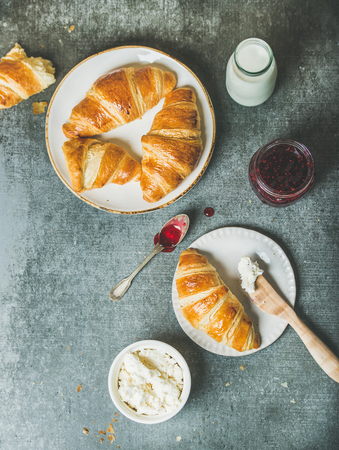 Breakfast concept. Freshly baked croissants with raspberry jam, cream cheese and milk in bottle over grey concrete background, top view, copy spaceの写真素材