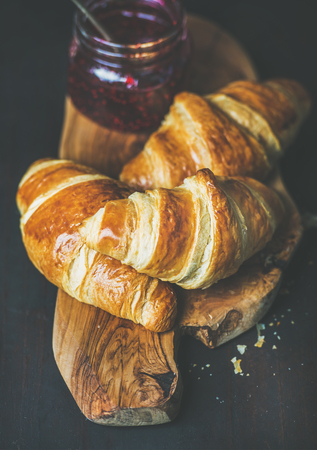 Breakfast concept. Freshly baked croissants with raspberry jam in jar on rustic wooden board over dark background, selective focusの写真素材