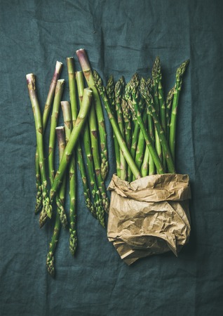 Fresh green asparagus in craft paper bag over dark grey linen table cloth background, top viewの写真素材