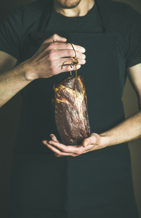 Man in black apron keeping cut of cured pork meat in his hands at local farmers market. Gourmet, organic food conceptの写真素材
