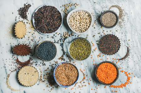 Variety of raw uncooked grains, beans, cereals in bowls, cups and baking molds for healthy cooking over marble background, top view. Clean eating, healthy, detox, vegan, vegetarian food conceptの写真素材
