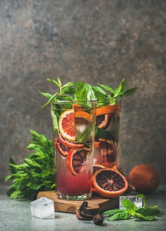 Blood orange citrus lemonade with mint and ice in tall glasses, dark brown stone background, copy space. Refreshing summer drink conceptの写真素材