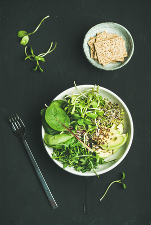 Green vegan breakfast meal in bowl with spinach, arugula, avocado, seeds and sprouts and crispy bread over black background, top view. Clean eating, dieting, vegan, vegetarian food conceptの写真素材