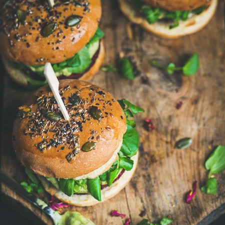 Healthy vegan burgers with beetroot and quinoa patty, arugula, avocado sauce, wholegrain bun on rustic wooden board over dark background, selective focus, copy space, square crop. Detox food conceptの写真素材