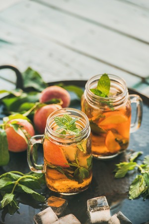 Summer refreshing cold peach ice tea with fresh mint in glass jars on metal tray over rustic wooden garden table, selective focus, copy spaceの写真素材