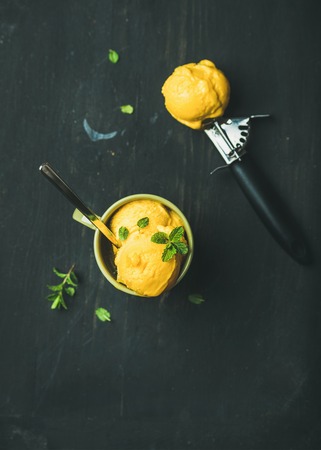 Refreshing summer dessert. Mango sorbet ice cream scoops with fresh mint in green cup over black wooden background, top view, copy space. Clean eating, healthy, vegetarian, alkaline diet food conceptの写真素材
