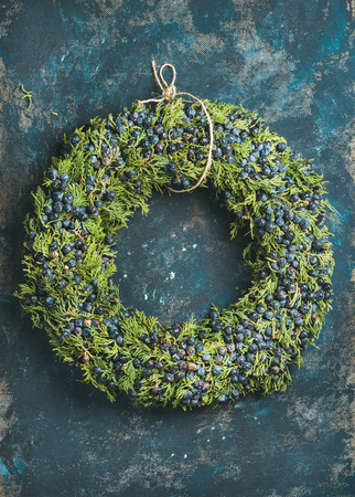 Christmas decorative green wreath with fresh blueberries and natural herbs over dark blue shabby plywood wall background, vertical compositionの写真素材