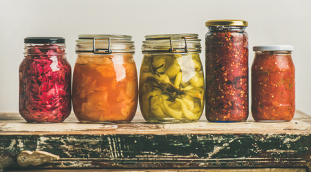 Autumn seasonal pickled or fermented vegetables in jars placed in row over vintage kitchen drawer, white wall background, copy space. Fall home food preserving or canningの写真素材