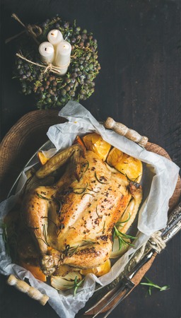 Christmas holiday table set with oven roasted whole chicken stuffed with oranges, bulgur and rosemary, decorative candles over dark wooden background. Top view, copy space, Slow food conceptの写真素材