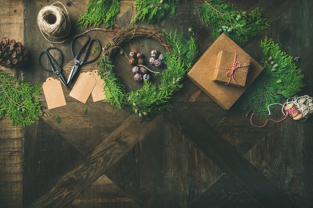 Preparing for Christmas or New Year holiday. Flatlay of fur tree branches, gift boxes, wreaths, rope, pine cone, scissorsand stickers over rustic wooden table bbackground, top view, copy spaceの写真素材