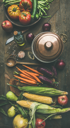 Fall cooking background. Autumn ingredients for Thanksgiving day dinner preparation. Flat-lay of green beans, corn cobs, carrot, tomatoes, eggplant, pears, apples over rustic wooden table, top viewの写真素材