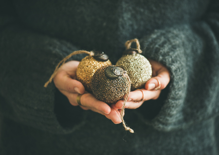 Woman in grey warm woolen sweater holding toy golden and silver decorative balls in hands, copy space, selective focus. Christmas, new year holiday celebration conceptの写真素材