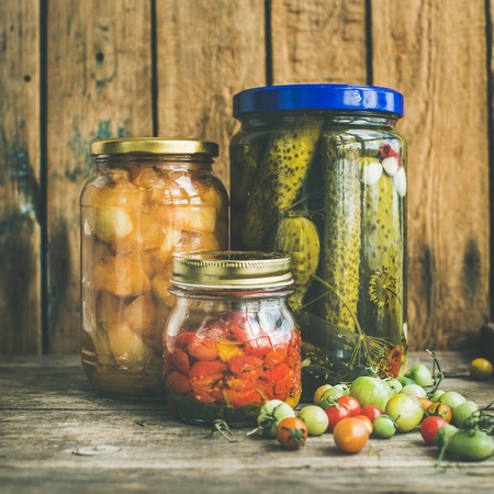 Autumn seasonal pickled vegetables and fruit in glass jars, rustic wooden barn background. Fall preserved vegetarian food concept, square cropの写真素材