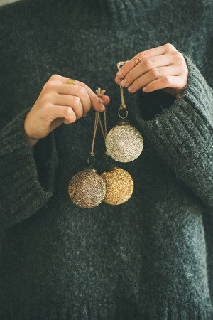 Woman in grey warm woolen sweater holding toy golden and silver decorative balls in hands, copy space. Christmas, new year holiday celebration conceptの写真素材