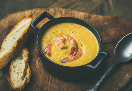 Corn creamy soup with shrimps served in individual pot with bread on board over rustic dinner table. Slow food, winter warming food conceptの写真素材