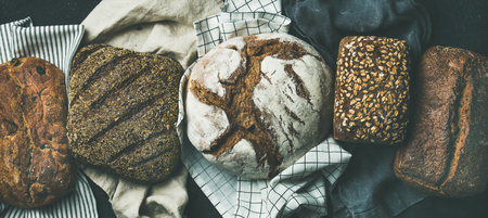 Various bread selection flat-lay. Top view of Rye, wheat and multigrain rustic bread loaves over black background, wide compositionの写真素材