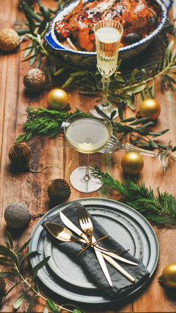 Christmas or New Year celebration table setting. Roast chicken or turkey, plates, silverware, champagne and toy holiday decoration over rustic wooden background, selective focusの写真素材