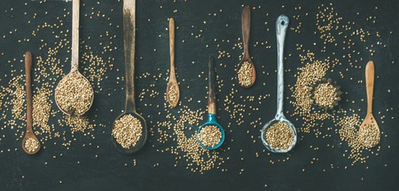 Flat-lay of various old vintage kitchen spoons full of green uncooked buckwheat grains over black stone background, top view, copy space, wide composition. Rustic cooking conceptの写真素材