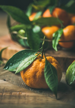 Christmas or New Year table. Fresh ripe tangerine with leaves over rustic wooden table background, selective focus, vertical composition, close-upの写真素材