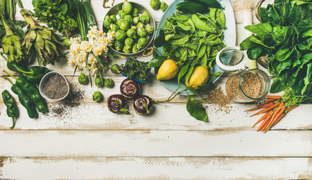 Spring healthy vegan food cooking ingredients. Flat-lay of vegetables, fruit, seeds, sprouts, flowers, greens over white wooden background, top view, copy space. Clean eating, diet food conceptの写真素材