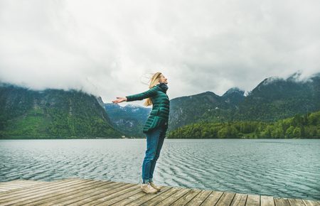 Relaxed female traveller with her arms open, standing at mountain lake coast enjoying the view of the Alps in Austria. Freedom conceptの写真素材