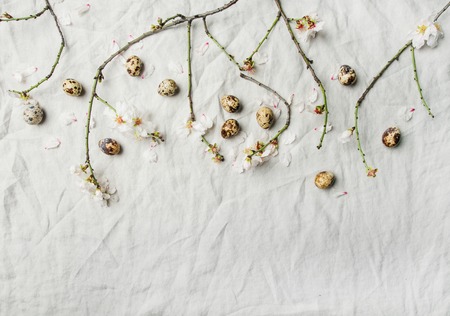Easter holiday background. Fkat-lay of tender Spring almond blossom flowers on branches and quail eggs over light grey linen cloth, top view, copy space. Greeting card conceptの写真素材