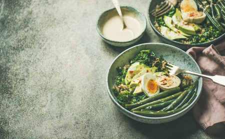 Healthy vegetarian breakfast bowls. Quinoa, kale, green beans, avocado, egg and creamy tahini dressing bowls over grey concrete background, selective focus, copy space. Energy boosting food conceptの写真素材