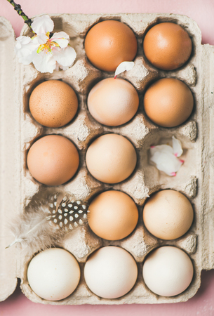 Easter holiday background. Flat-lay of gradient natural colored eggs in box with tender Spring almond blossom flower and feather over light pink background, top view. Greeting card conceptの写真素材