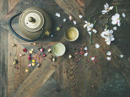 Traditional Asian tea ceremony arrangement. Flat-lay of iron teapot, cups, dried rose buds and blooming almond tree flowers over wooden table background, top view, copy spaceの写真素材