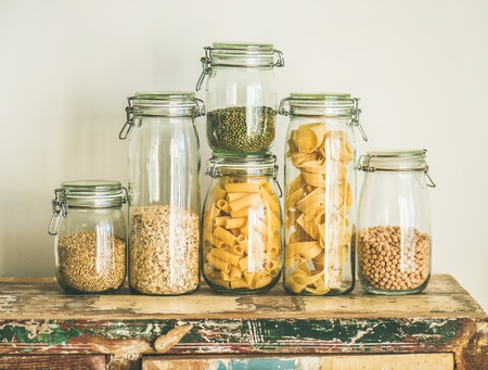 Various uncooked cereals, grains, beans and pasta for healthy cooking in glass jars on rustic wooden table, white background. Clean eating, vegetarian, vegan, balanced dieting food conceptの写真素材