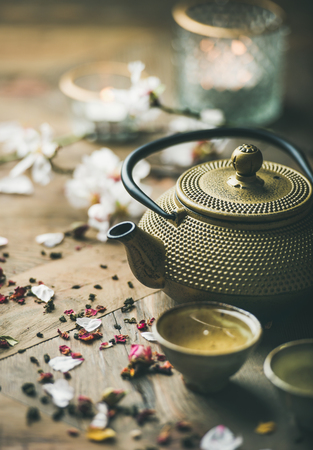 Traditional Asian tea ceremony arrangement. Iron teapot, cups, blooming almond flowers, dried rose buds and candles over wooden table background, selective focusの写真素材