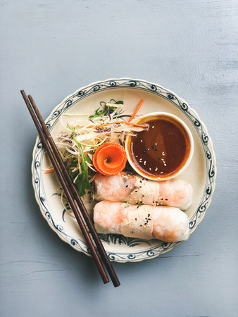 Asian style dinner. Flat-lay of summer rice paper rolls with shrimp and teriyaki sauce in bowl over...