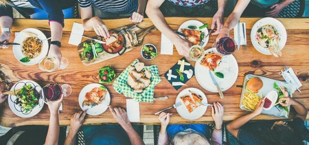 Family or friends summer party or outdoor dinner. Flat-lay of group of people at big table in cafe eating verious food together. Summer gathering or celebration conceptの写真素材