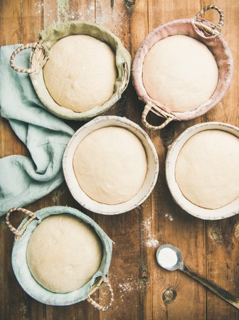 Sourdough for baking homemade wheat flour bread in baskets, over rustic wooden kitchen table backgroundの写真素材