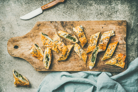 Flat-lay of fresh Turkish borek roll with spinach, feta cheese, black cumin seeds cut in slices on rustic wooden board over concrete background, top view. Traditional East Mediterranean cuisineの写真素材